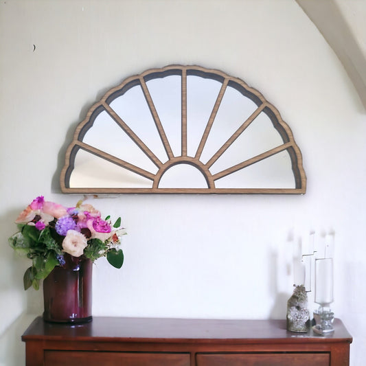 Art Deco style semi-circular wood framed fan mirror hanging on a white wall above a wooden console table.