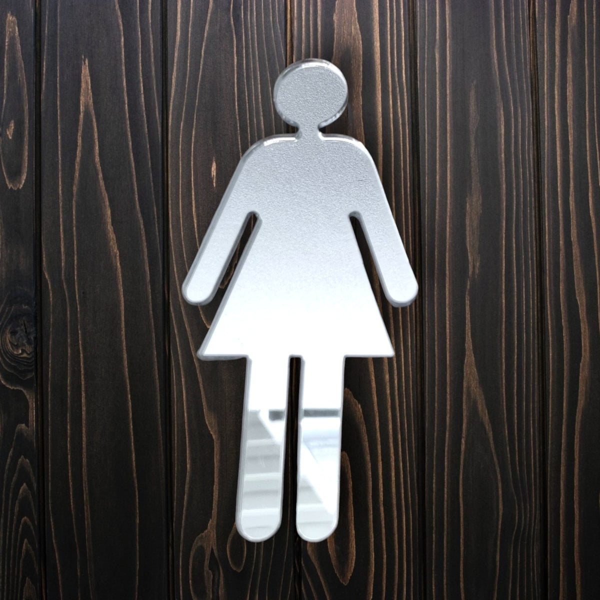Mirrored female toilet sign mounted on dark vertical wooden panels.