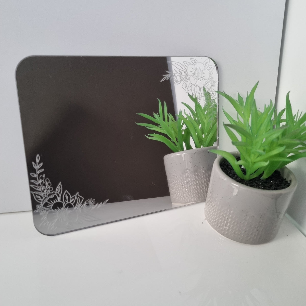 Floral etched rectangular mirror with rounded corners, featuring white etched flowers in opposite corners.