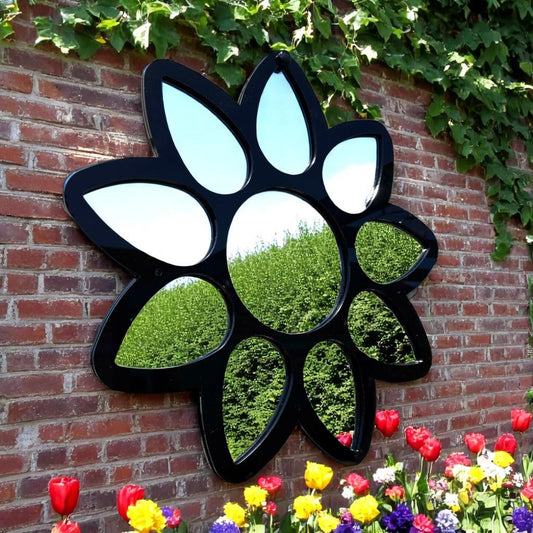 Black flower-shaped mirror with petal-like mirrored panels, mounted on a red brick wall.