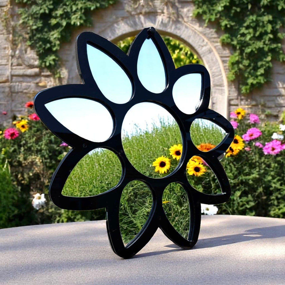 Black flower-shaped mirror with petal mirrors surrounding a central circular mirror, outdoors.