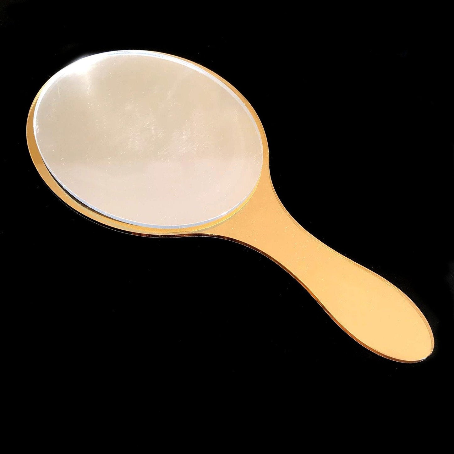 An oval hand-held mirror with a glossy gold-colored frame and handle against a black background.