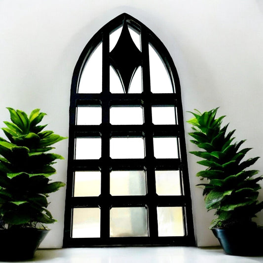 Black gothic arch garden mirror with a diamond frame, flanked by two potted green plants.