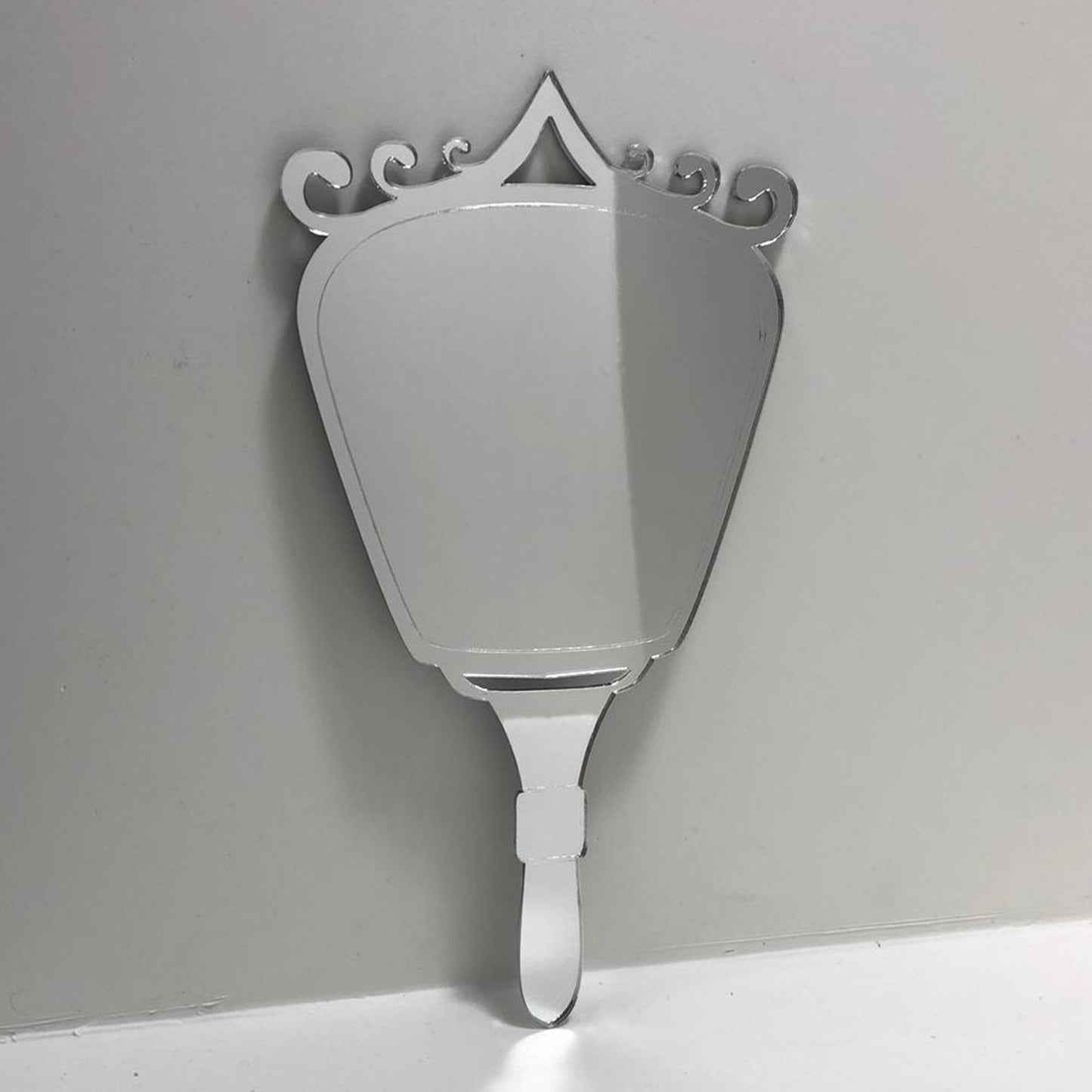 Silver Art Deco-style hand-held mirror with a fan-shaped glass body, ornate swirled top, and matching handle.