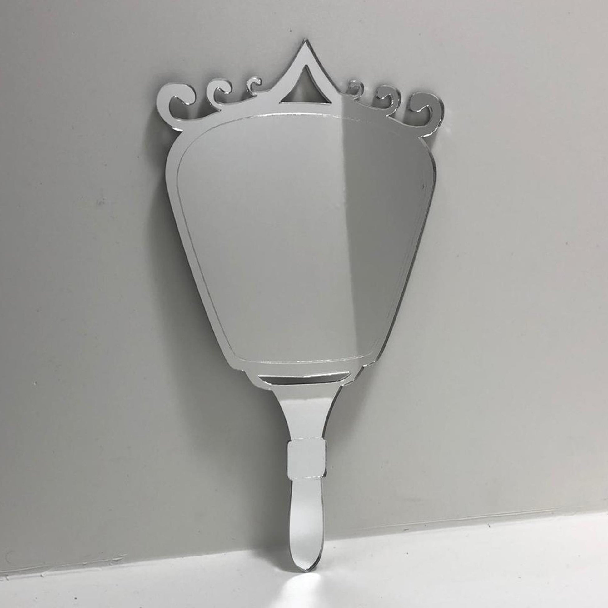 Silver Art Deco-style hand-held mirror with a fan-shaped glass body, ornate swirled top, and matching handle.