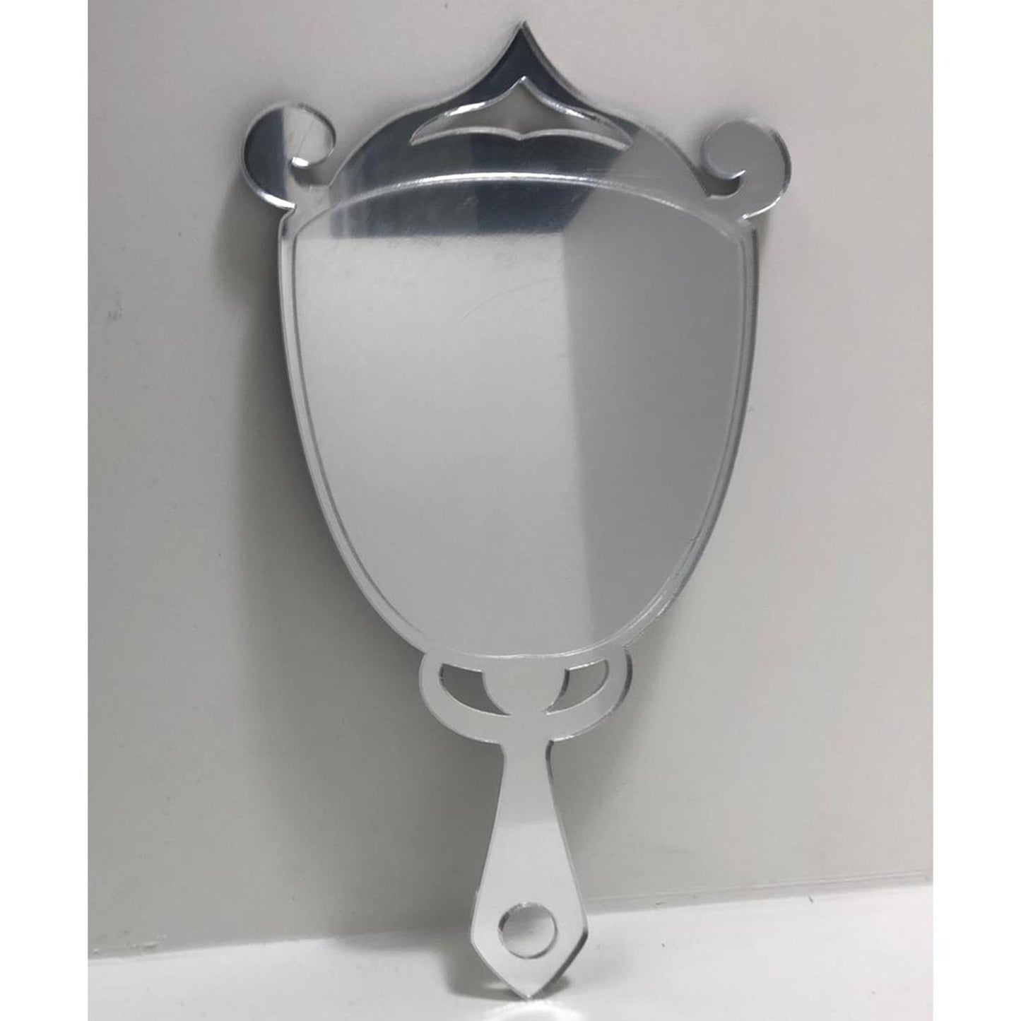 Art Deco trophy-shaped hand-held mirror with a mirrored finish, ornate top, scrolls, and a handle with a circular cutout.