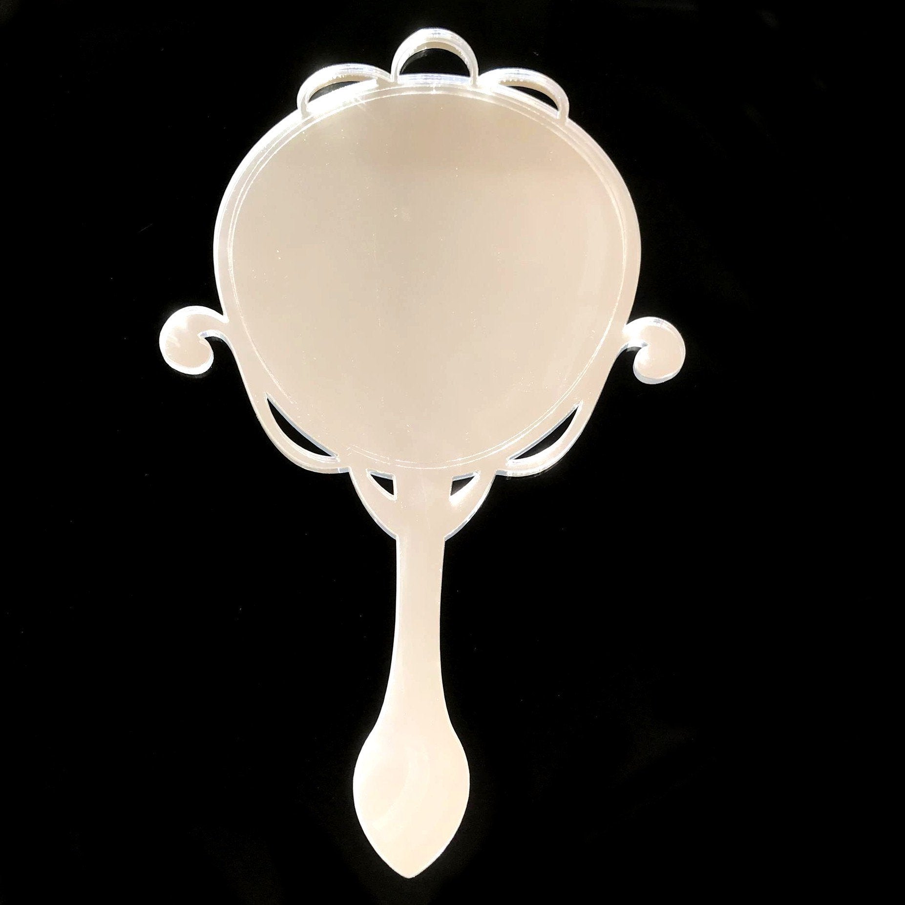 Arts and Crafts style oval hand held mirror with ornate scrollwork frame on black background.