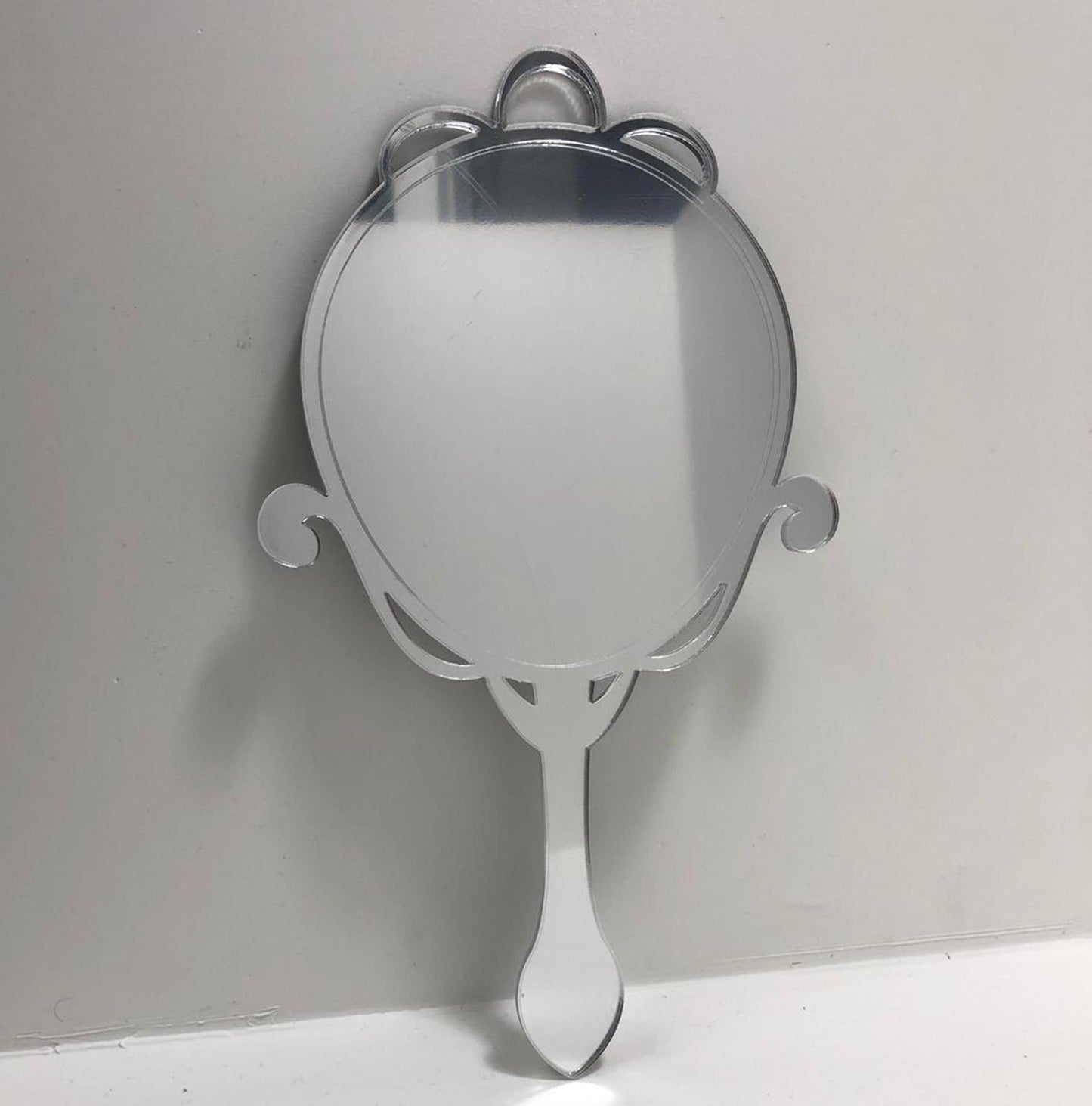 Arts and crafts oval hand-held mirror with ornate top and handle.