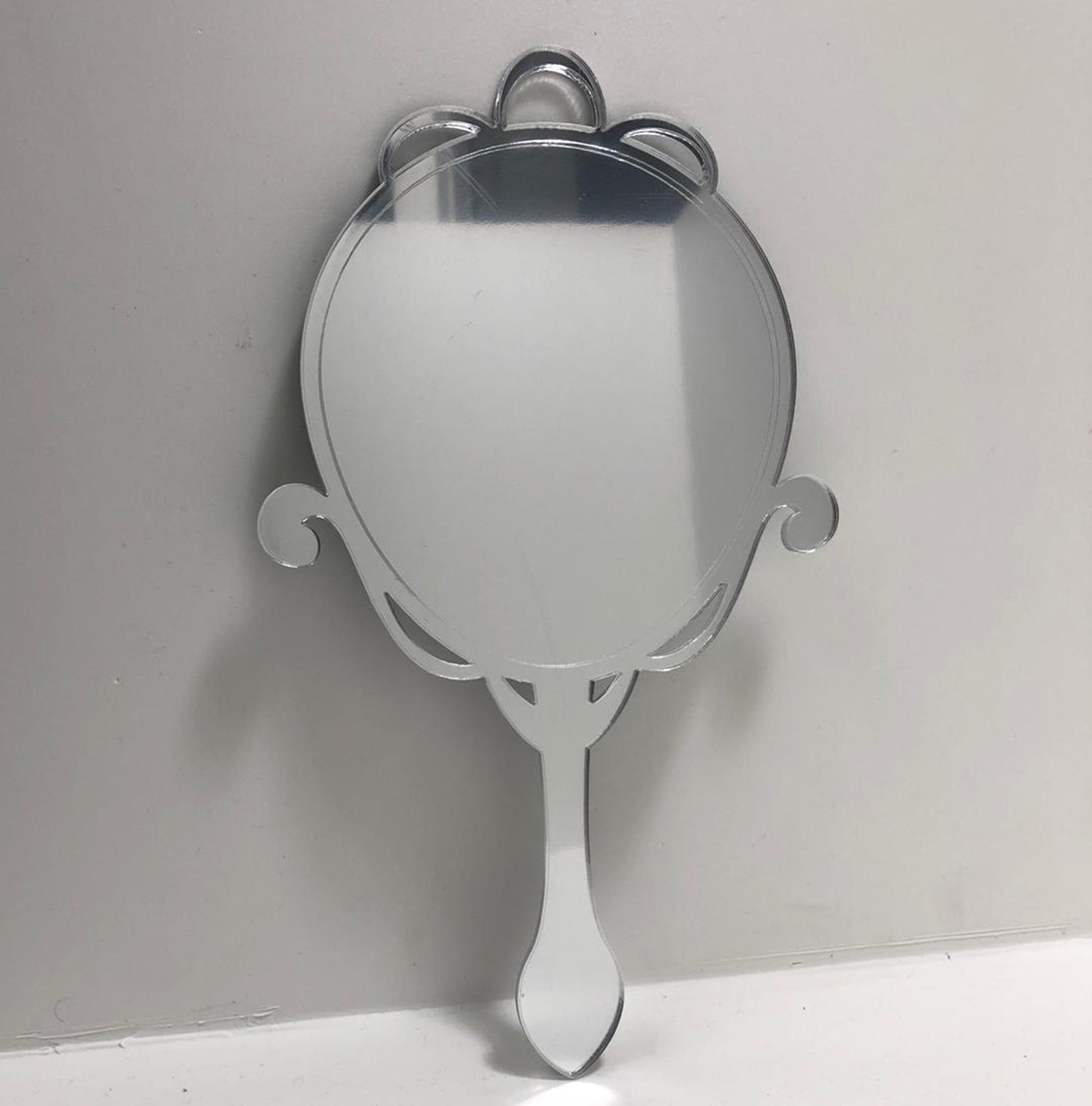 Arts and crafts oval hand-held mirror with ornate top and handle.