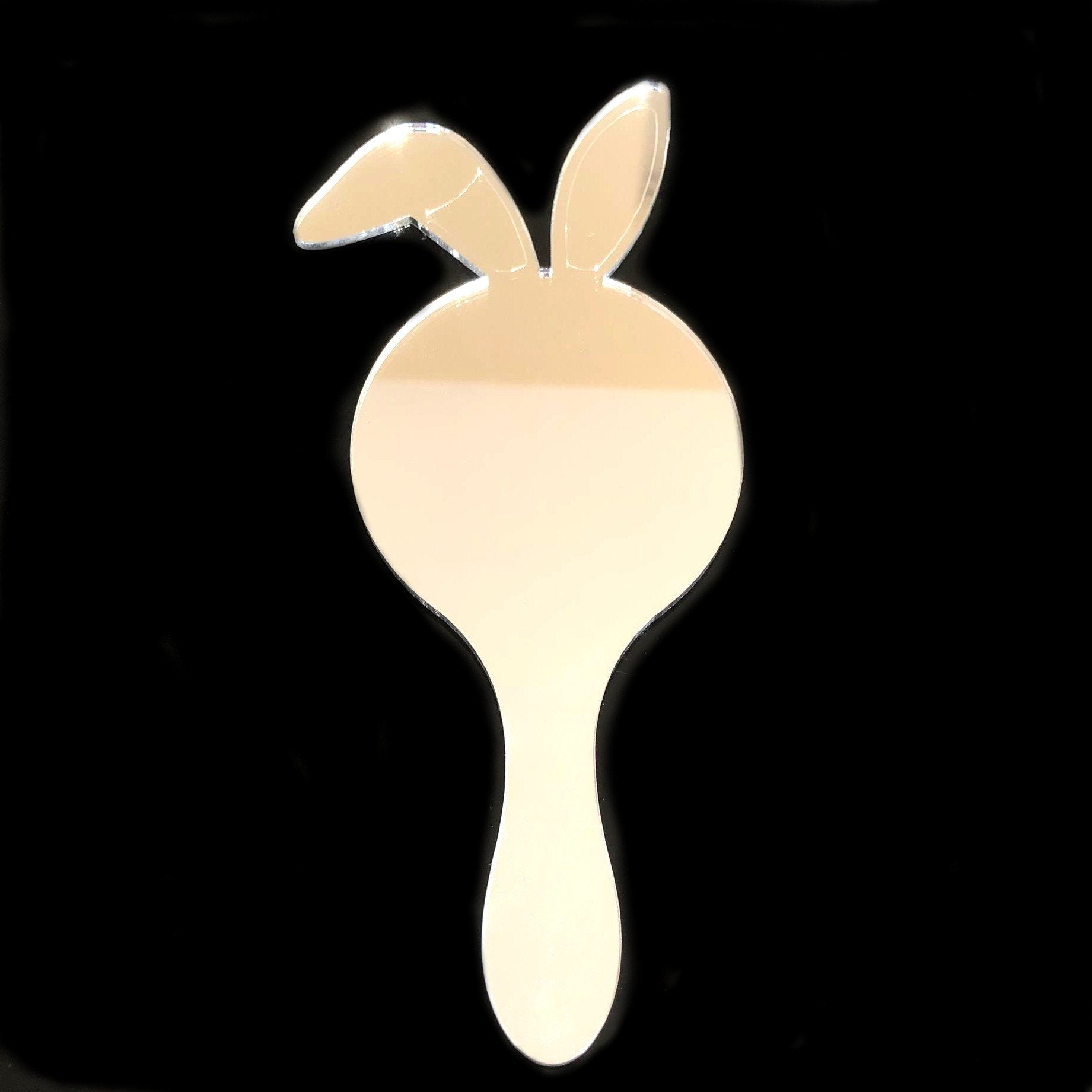 A bunny rabbit-shaped hand-held mirror with long ears and a handle against a black background.