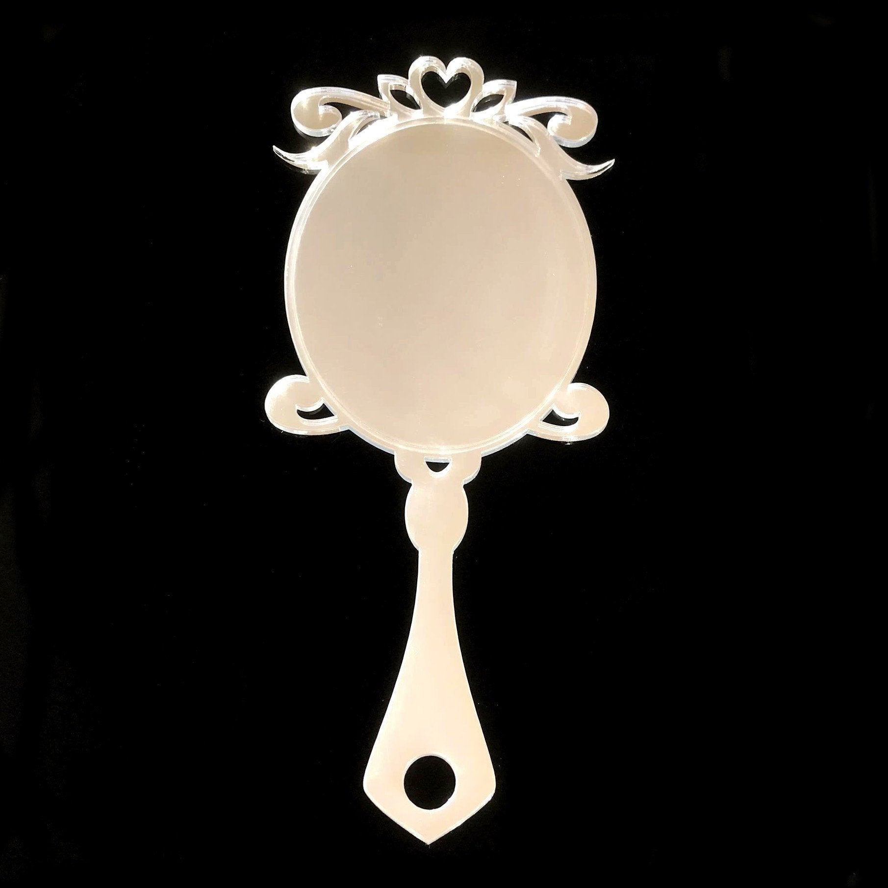 Georgian style oval handheld mirror made of clear acrylic, featuring ornate scrolling and a heart design.
