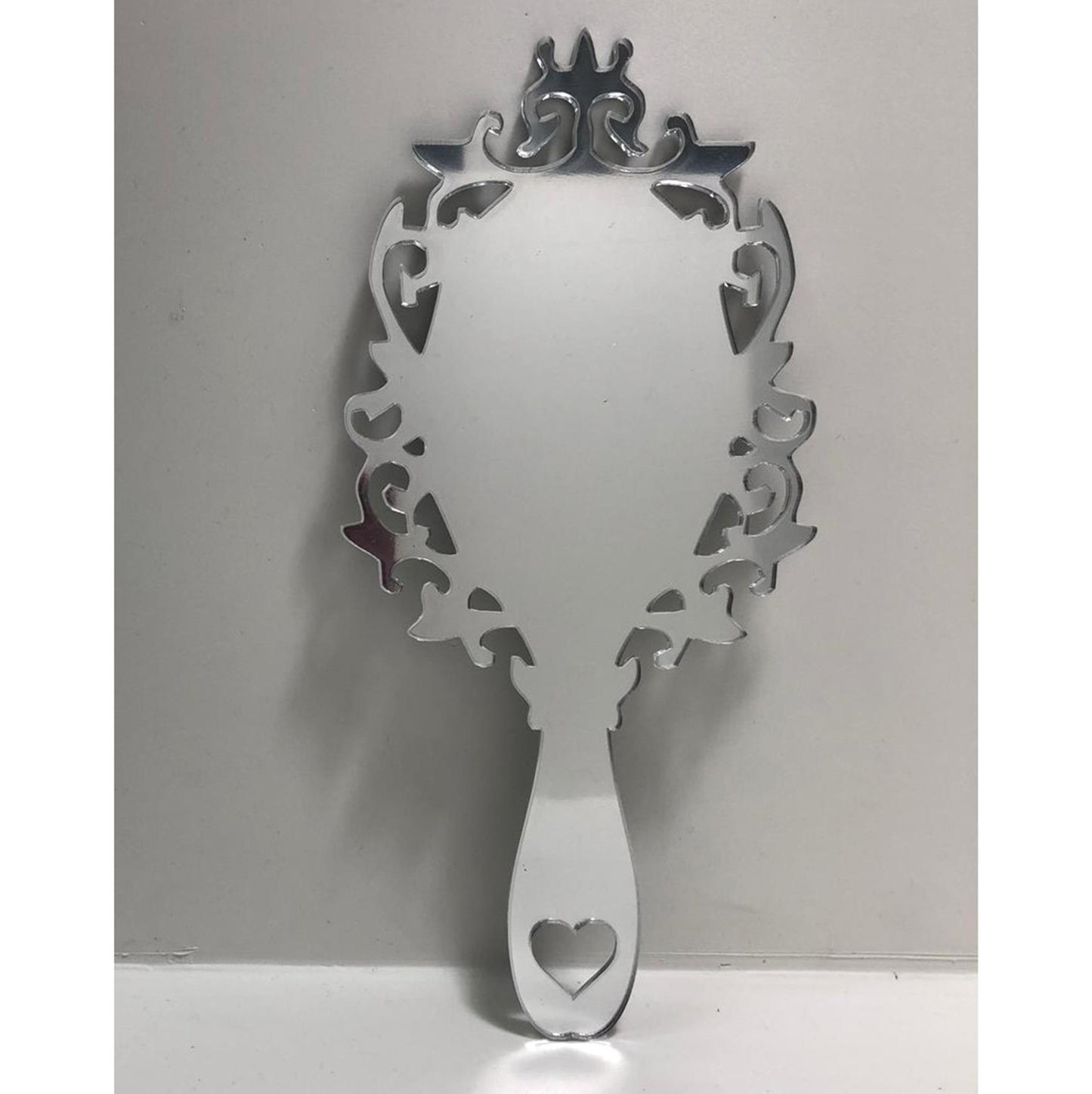 Victorian vintage-style silver hand-held mirror with ornate scrollwork frame and heart-shaped cutout on the handle.