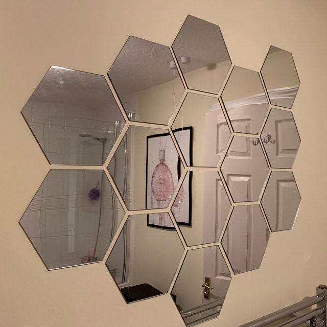 A cluster of eleven frameless hexagonal mirrors arranged in a honeycomb pattern on a beige wall.