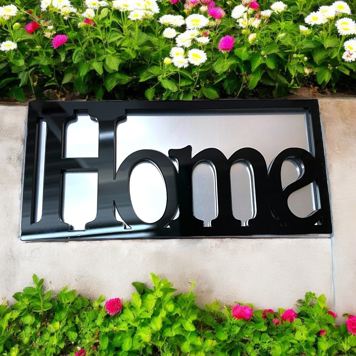 A rectangular framed garden mirror featuring the word "Home" in bold black lettering against a reflective surface.