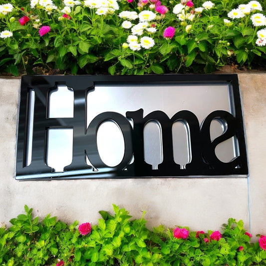 A rectangular framed garden mirror featuring the word "Home" in bold black lettering against a reflective surface.