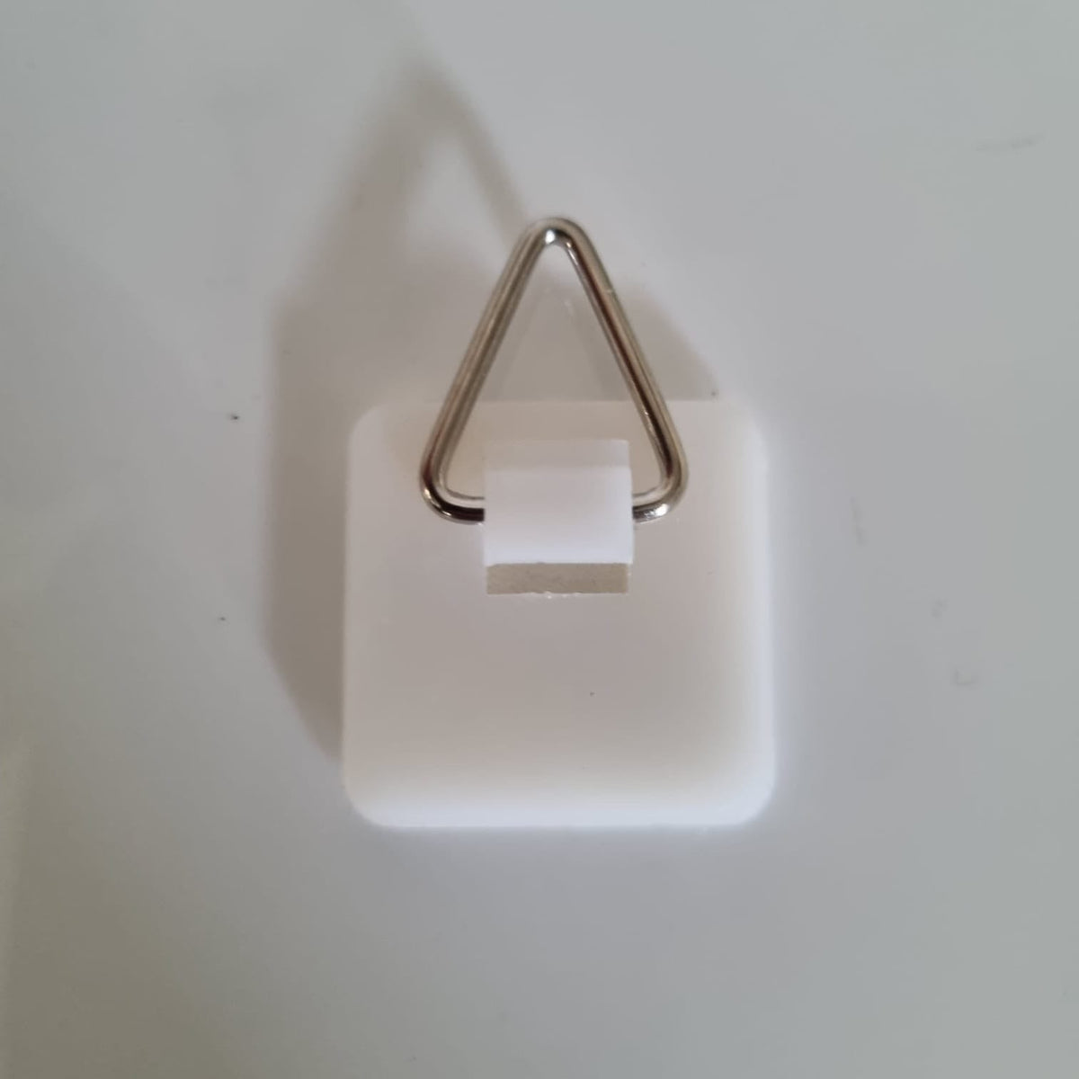 Close-up of a white plastic D-ring picture hanger hardware against a white background.