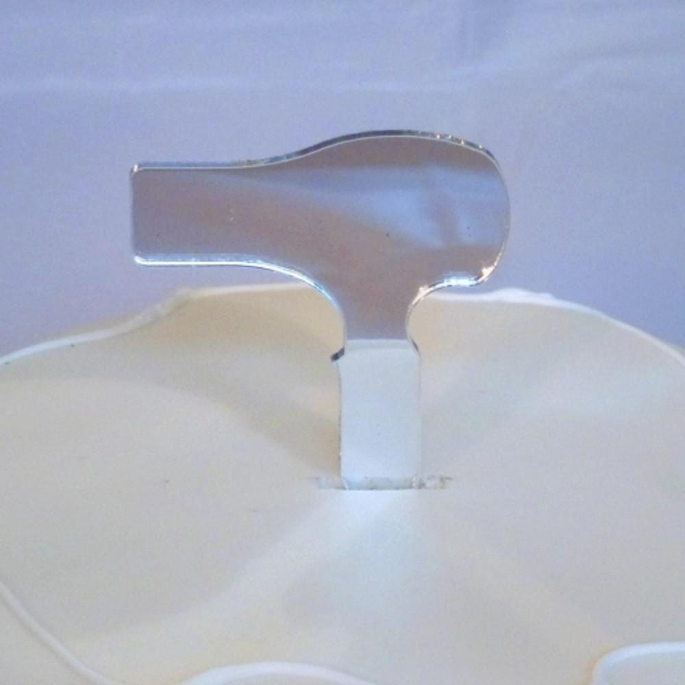 Shiny silver, mirror-finish hairdryer shaped acrylic cake topper inserted into a plain white frosted cake.