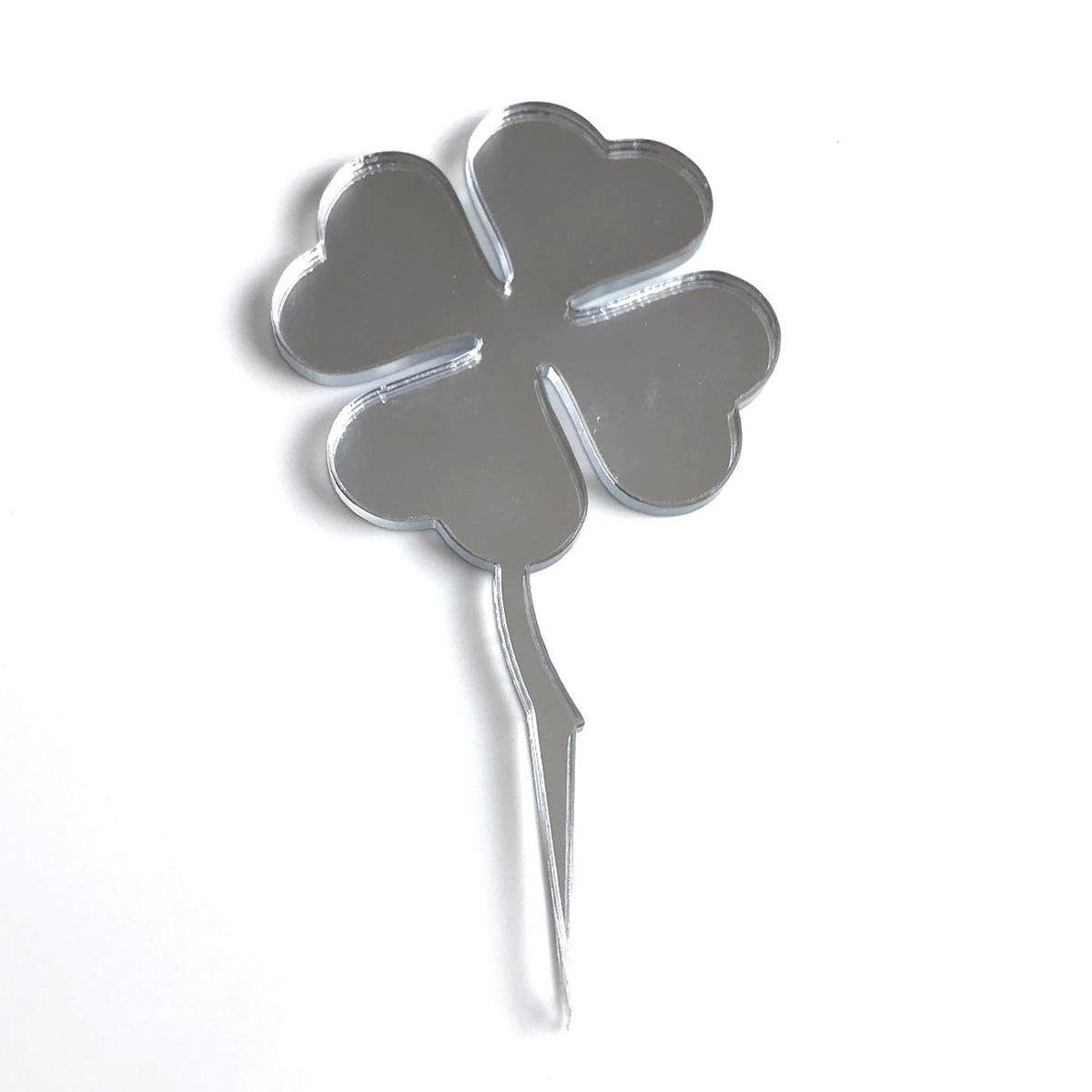 Silver mirrored acrylic four-leaf clover cupcake topper on a simple stick, isolated on a white background.