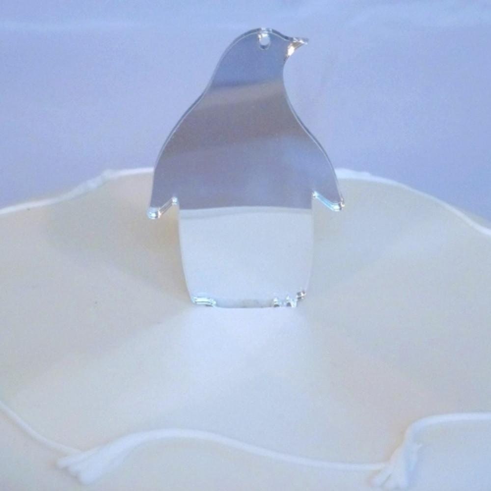 A shiny, silver, mirrored penguin-shaped cake topper standing on a plain white cake.