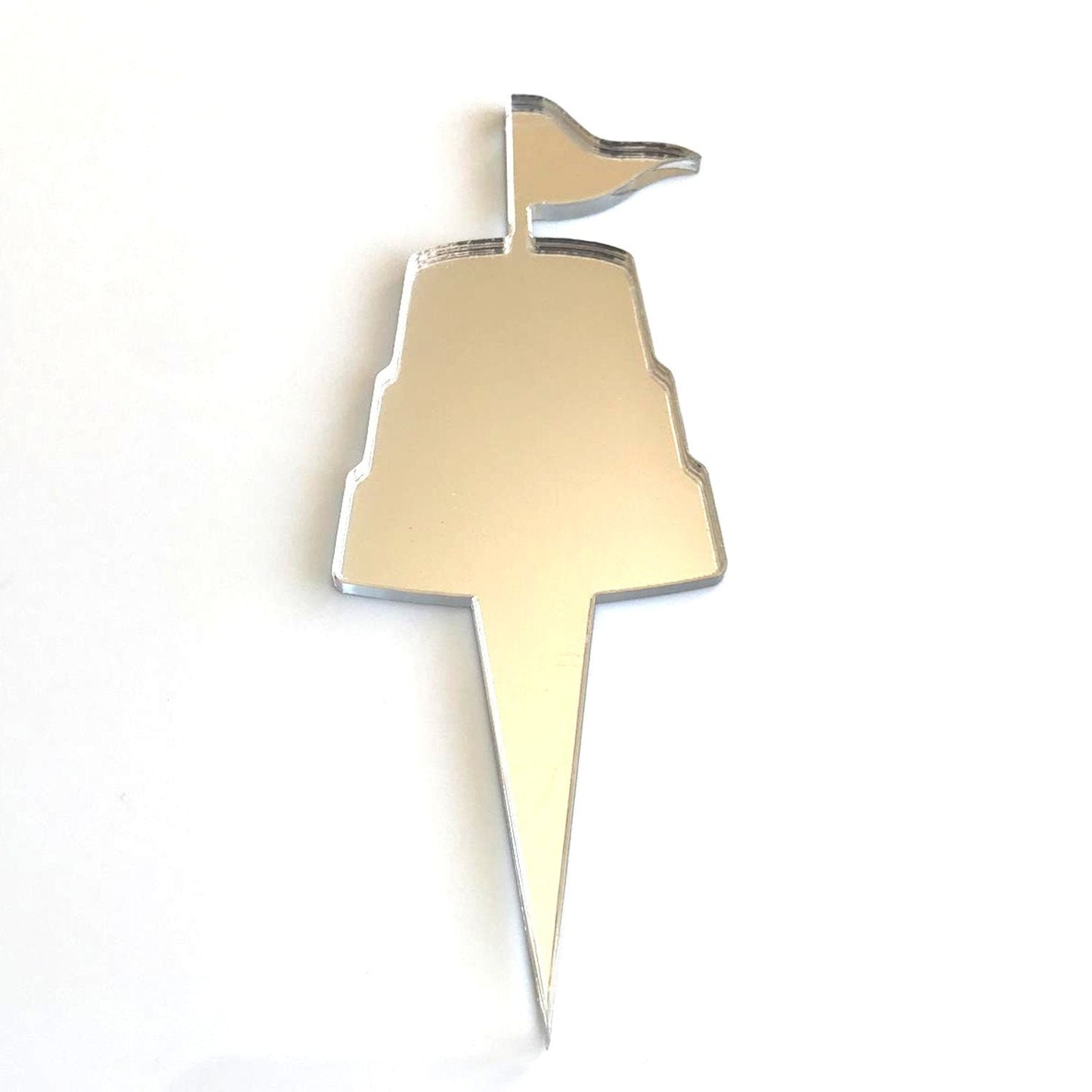Silver mirrored acrylic cake topper shaped like a sandcastle with a flag on a pointed stake.