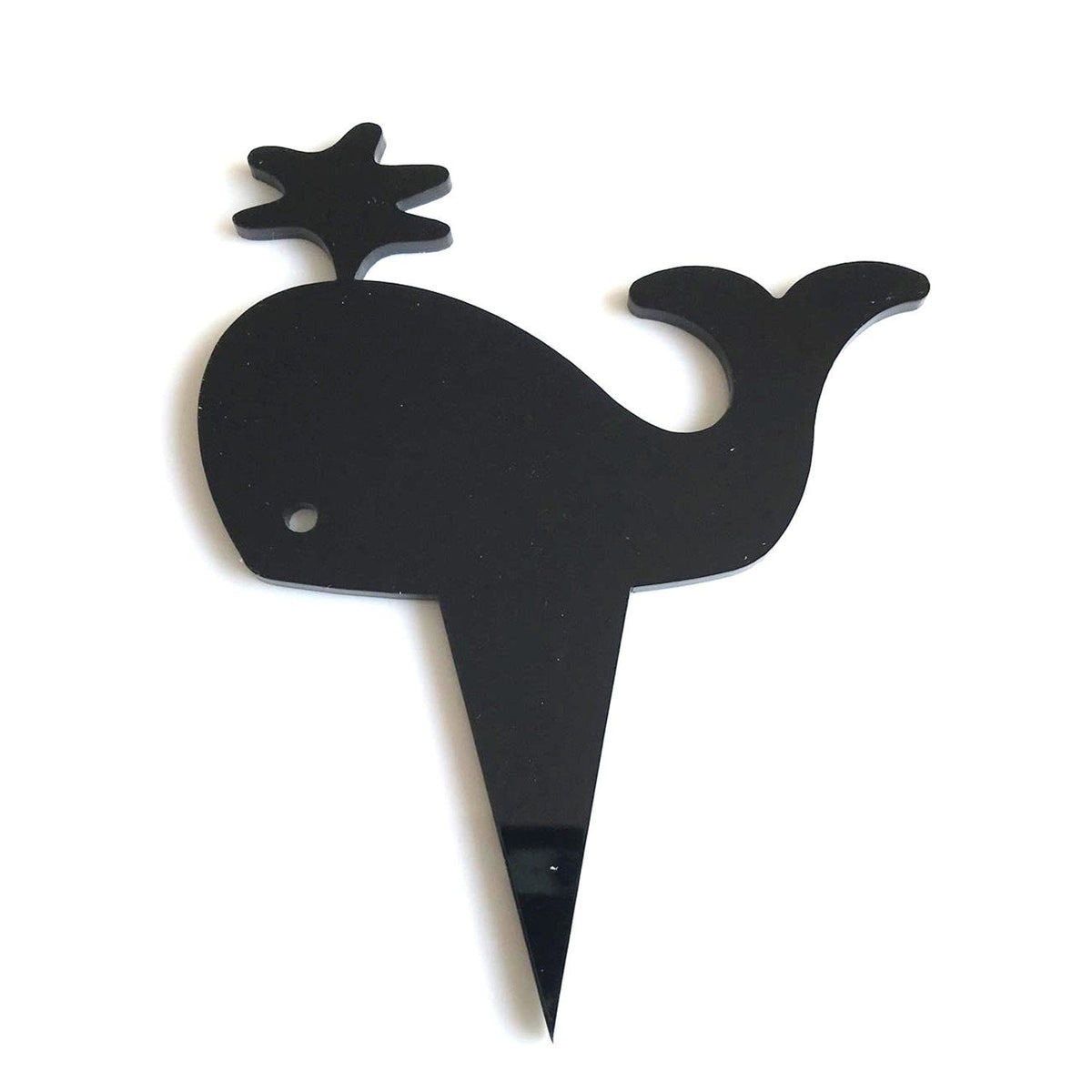 Black acrylic whale cupcake topper with a water spout silhouette on a pointed stake against a white background.