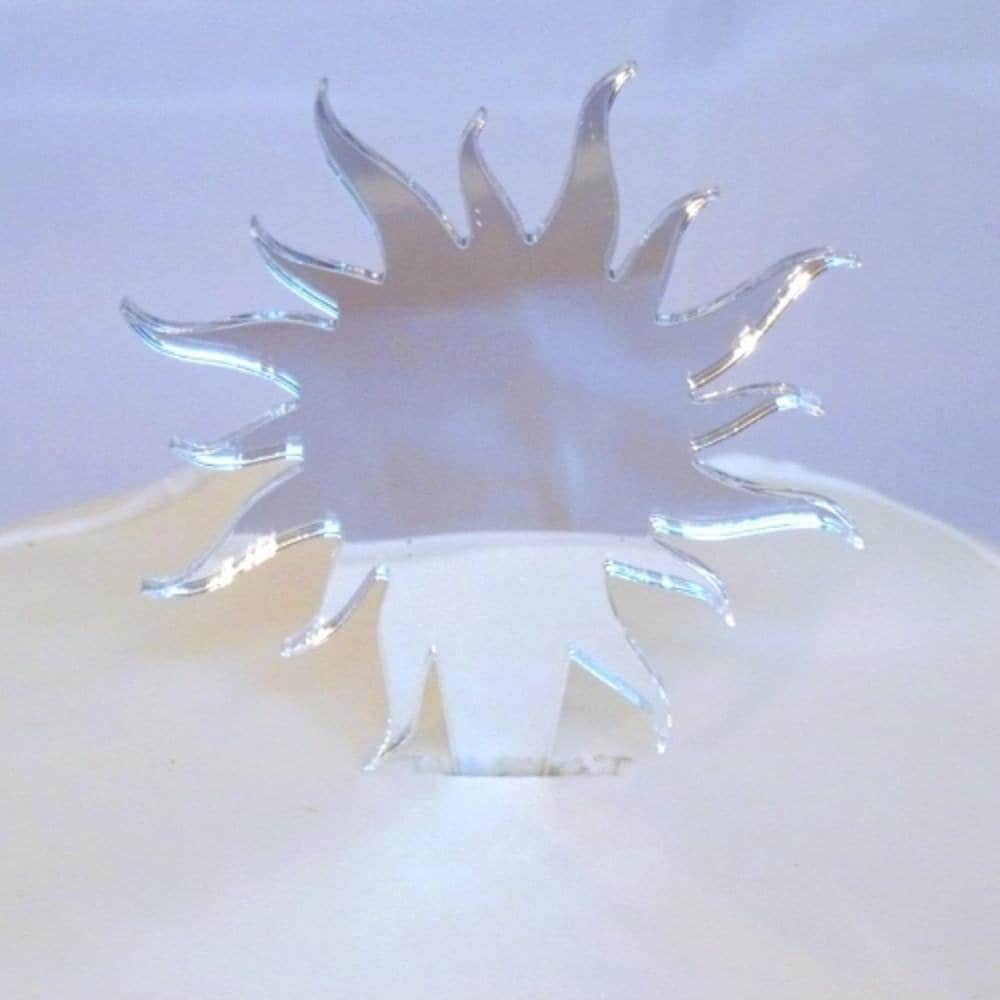 Clear, laser-cut sun-shaped cake topper with pointed, swirling rays, inserted into a white cake.