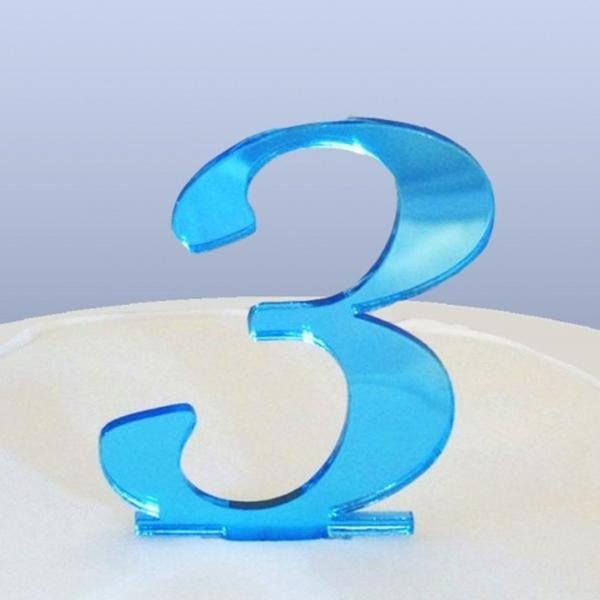 Shiny blue acrylic laser-cut cake topper in the shape of the number 3, standing on a white surface.