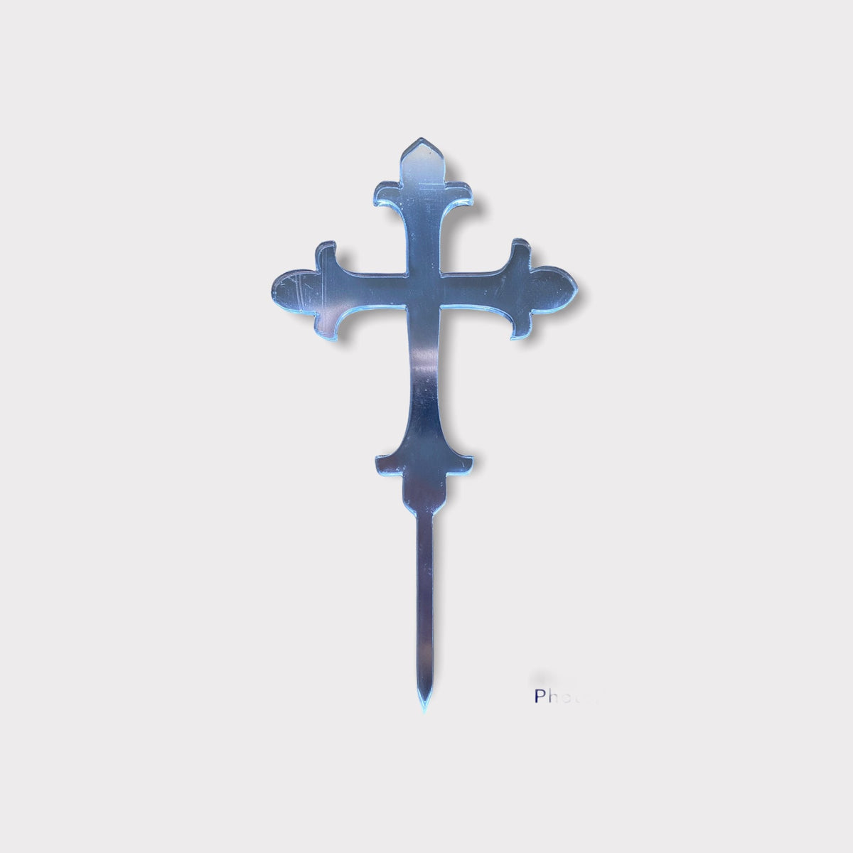 A mirrored, silver, laser-cut cross cake topper with a fleur-de-lis inspired design and a pointed stake.