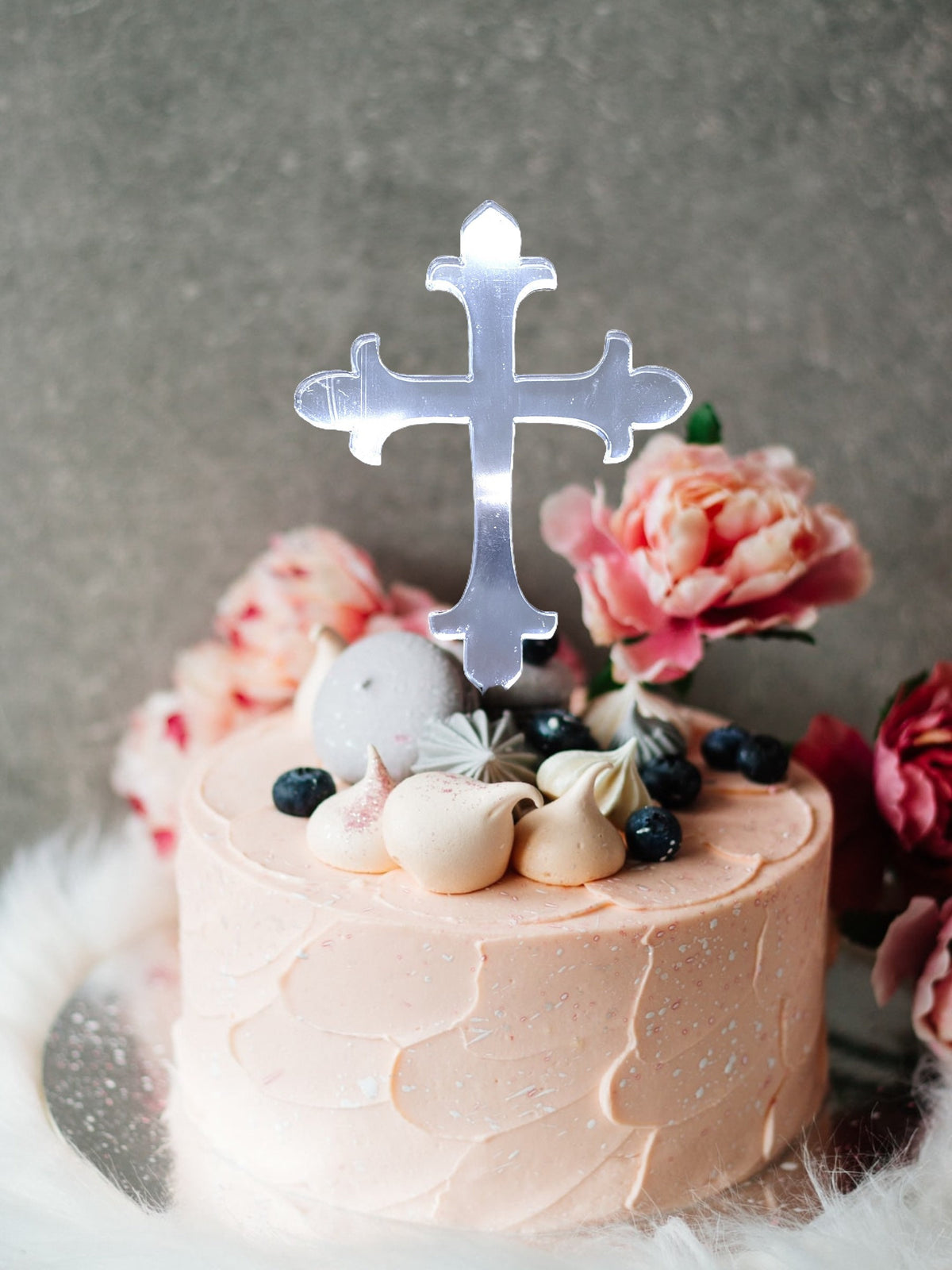 Clear, laser-cut acrylic cross cake topper styled on a peach-frosted cake with flowers and berries.