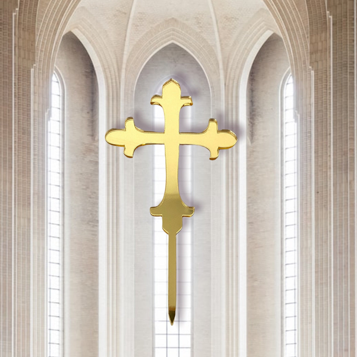 Gold mirror acrylic cross cake topper with fleur-de-lis style ends against a blurred church interior background.