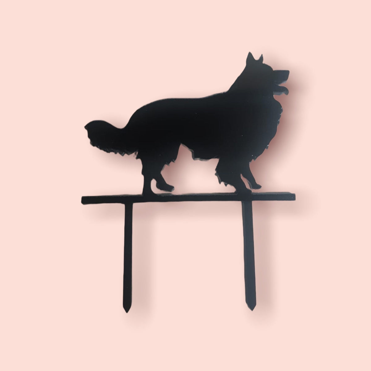 Black acrylic cake topper shaped like a standing long-haired dog silhouette on two pointed stems.
