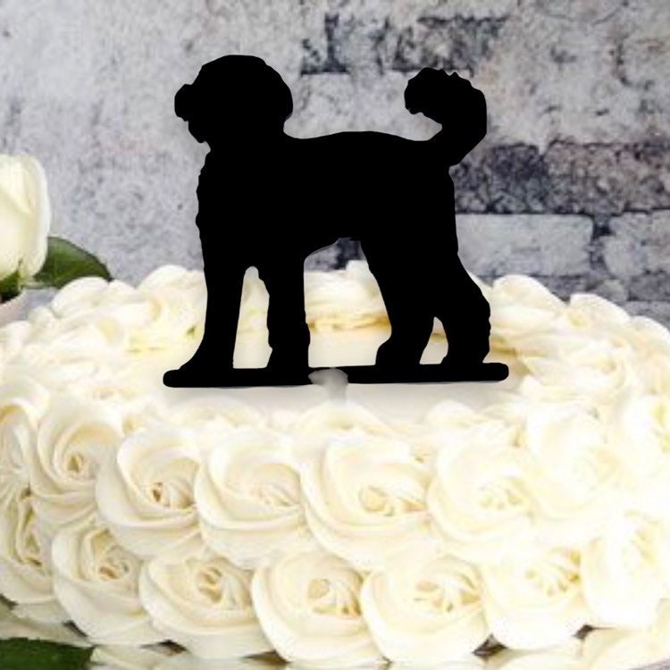 Black silhouette Cockapoo dog cake topper standing on a white frosted cake with rose swirls.