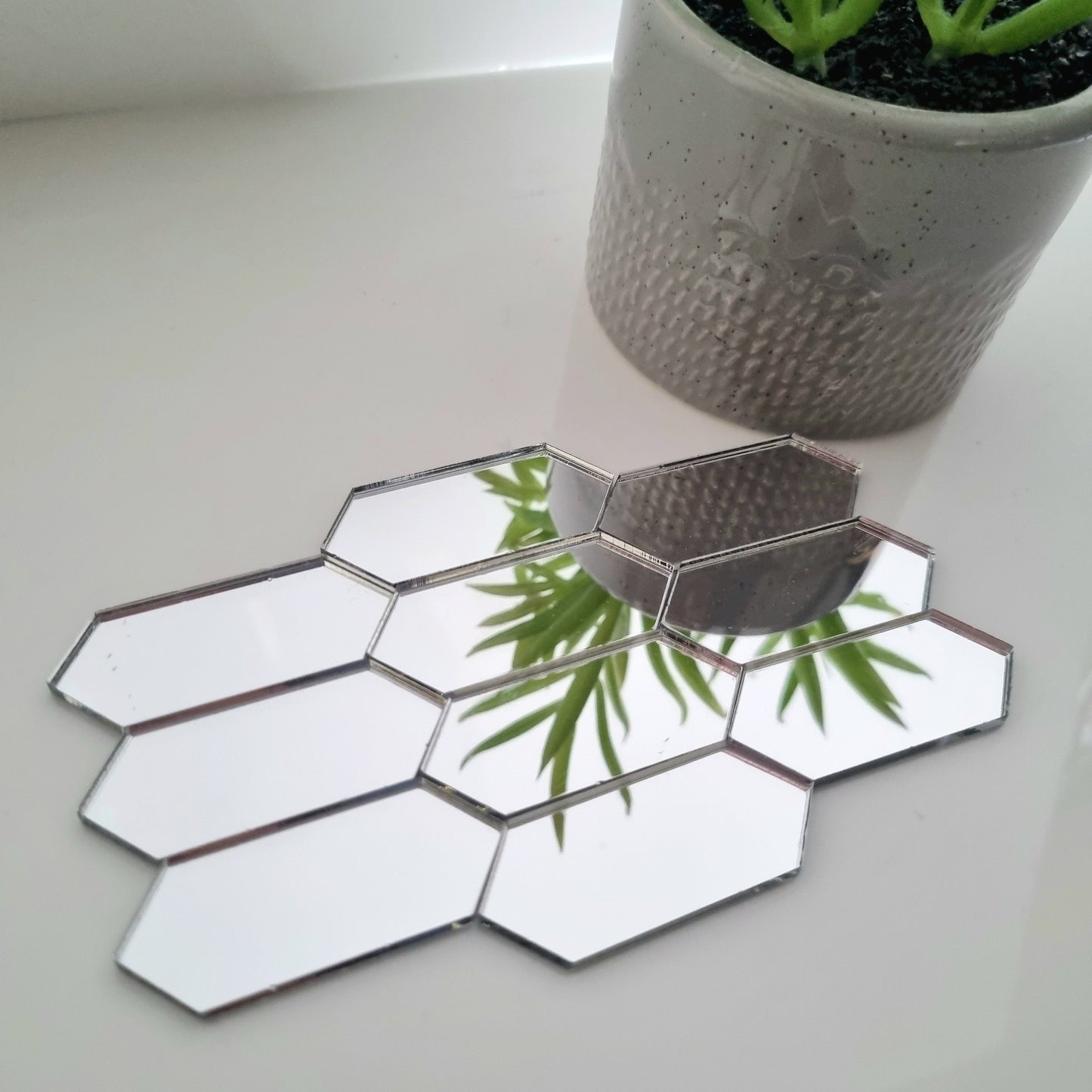 Silver acrylic mirror tiles shaped as elongated hexagons, arranged on a surface with a potted plant.