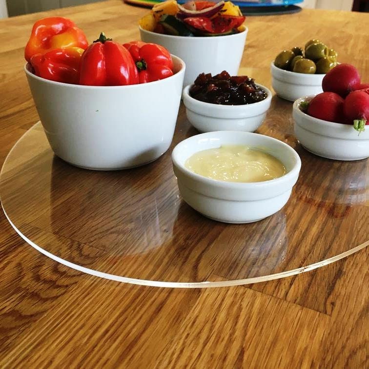 Clear oval acrylic table runner/worktop saver on a wooden table, supporting white bowls filled with food.