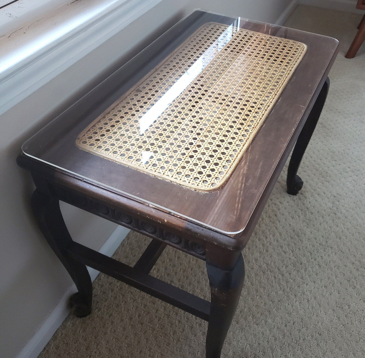 A rectangular, clear acrylic table protector sits atop a vintage wood side table with a caned inlay.