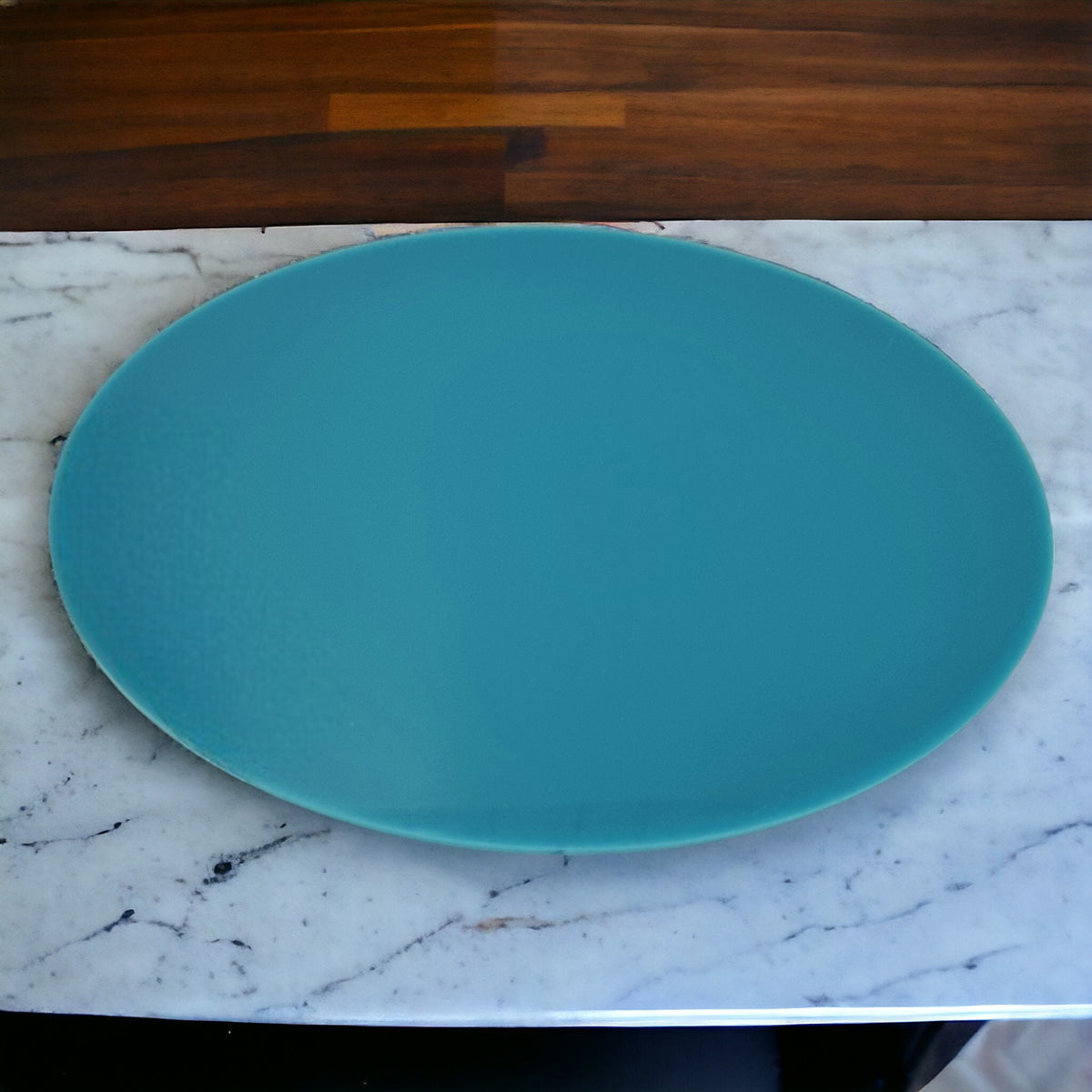 Oval, teal-colored acrylic worktop saver resting on a white marble surface.