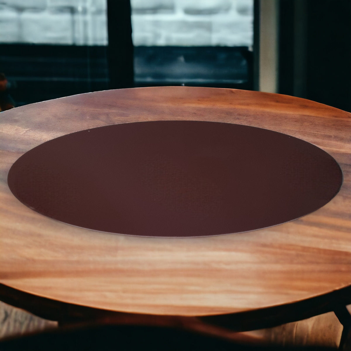A smooth, oval, dark brown acrylic worktop saver centered on a round wooden table.