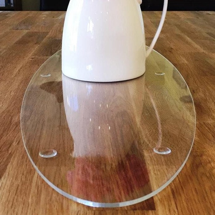 Clear oval acrylic table runner or worktop saver with small feet, sitting on a wooden table under a white pitcher.