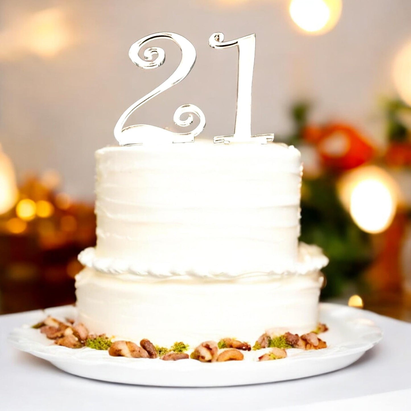 Shiny silver reflective "21" cake topper in a classic, elegant font style on a two-tier white frosted cake.
