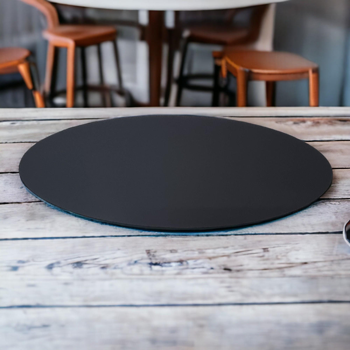 Matte black oval acrylic placemat centered on a rustic, weathered wooden tabletop.