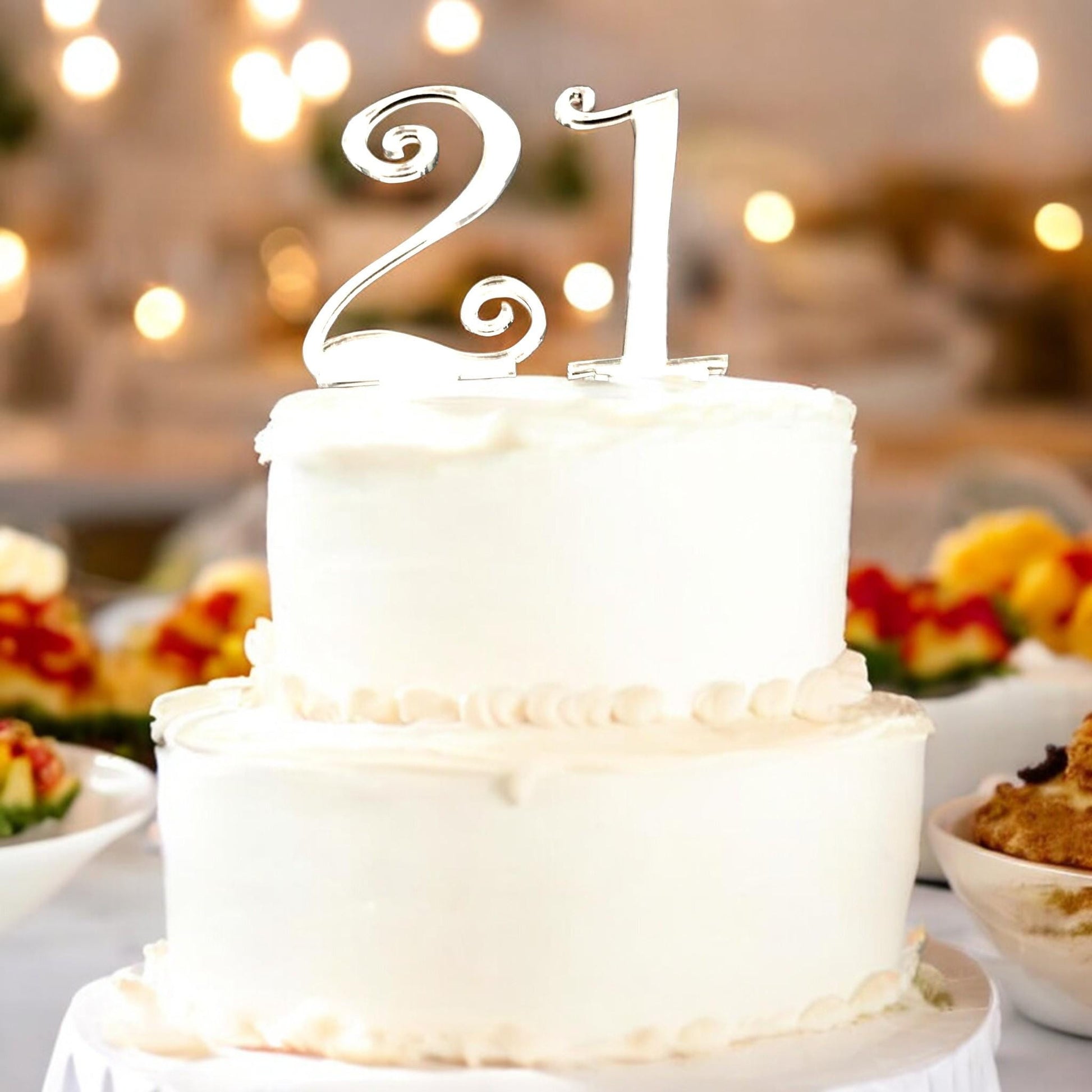 Shiny silver-toned acrylic cake topper featuring the number "21" in a stylized, elegant font on a white tiered cake.