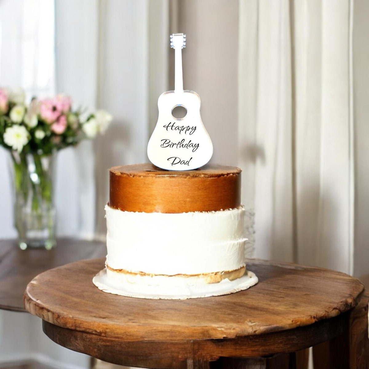 White acrylic acoustic guitar cake topper engraved with "Happy Birthday Dad" atop a two-tone cake.