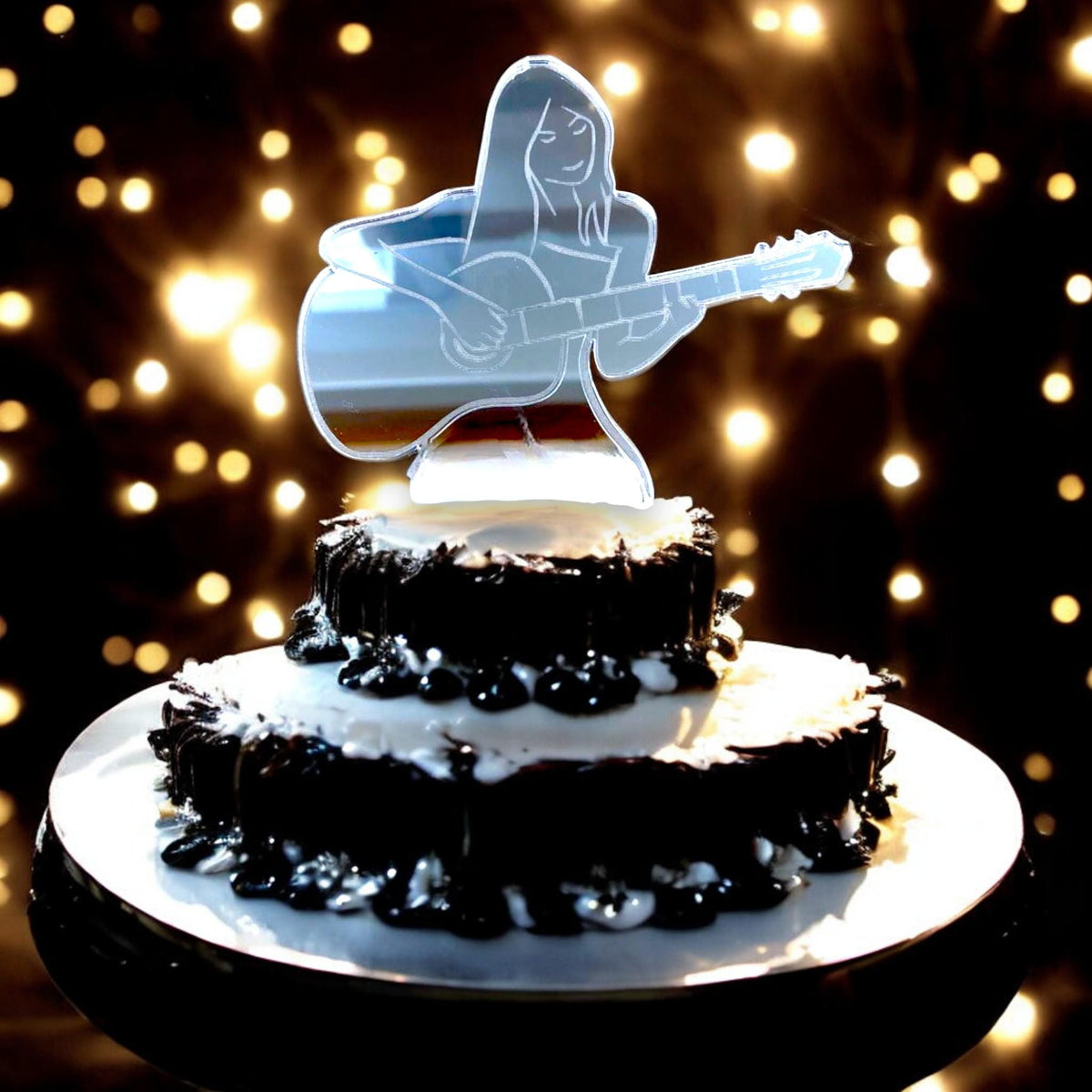 Mirror-finish acrylic cake topper of a woman playing an acoustic guitar, sitting atop a tiered chocolate cake.