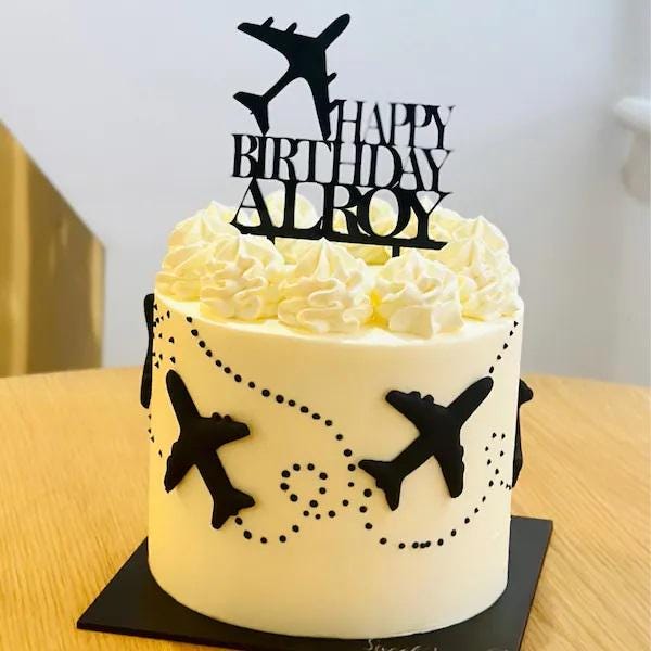 Black acrylic "Happy Birthday Alroy" cake topper with an aeroplane silhouette, atop a white frosted cake.
