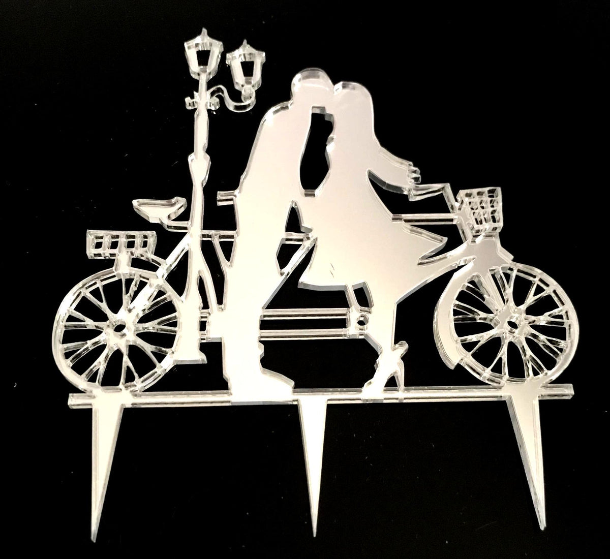Silver mirrored acrylic cake topper featuring a couple kissing by a bicycle and a streetlamp.