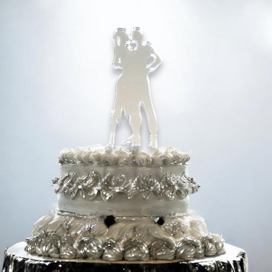 Clear acrylic silhouette cake topper of a dancing couple, standing atop a white two-tier decorated wedding cake.
