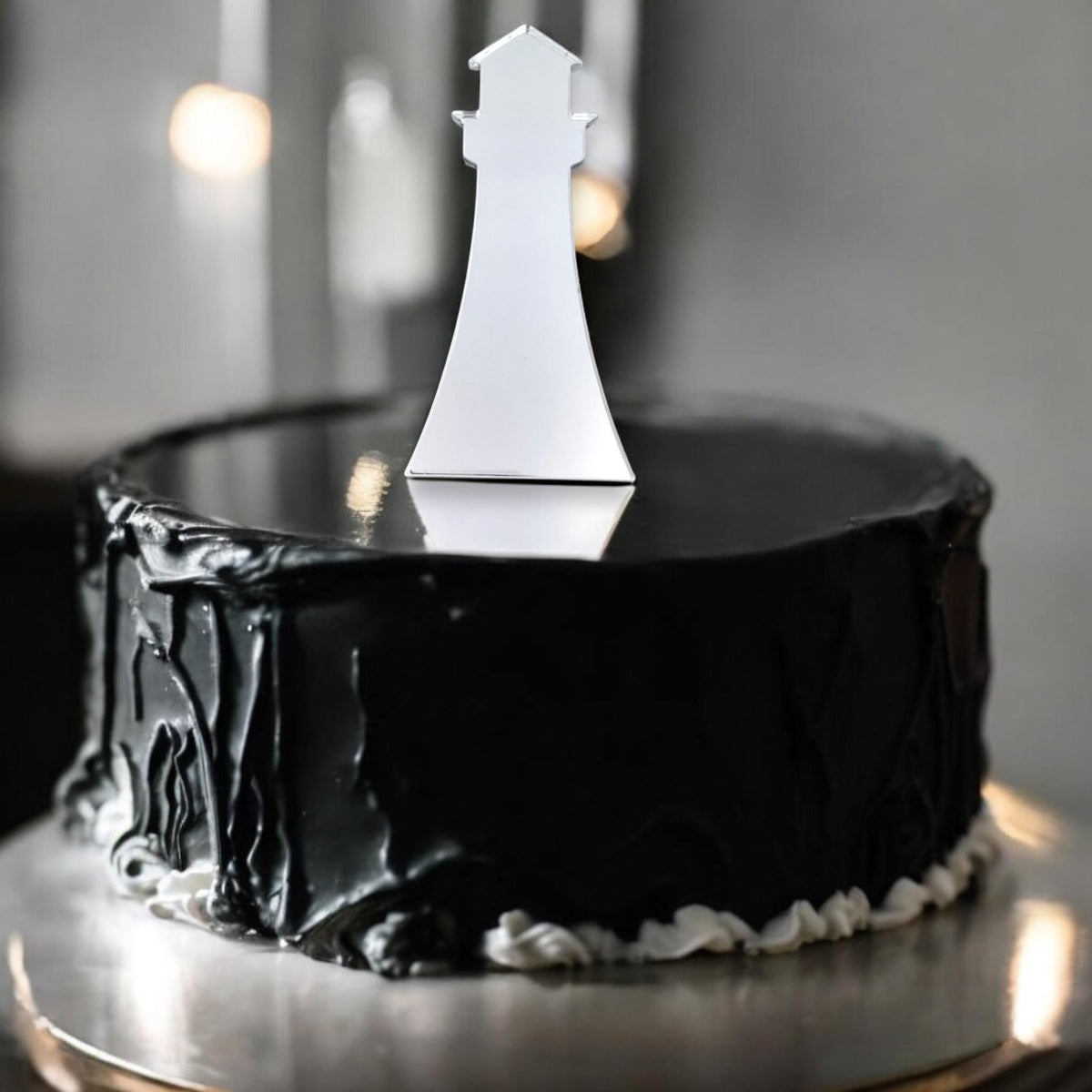 A reflective silver lighthouse cake topper sits atop a round, dark black cake with textured frosting.