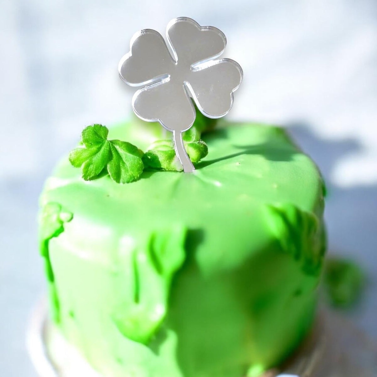 Shiny silver, mirror-finish acrylic four-leaf clover cupcake topper on a bright green frosted cupcake.