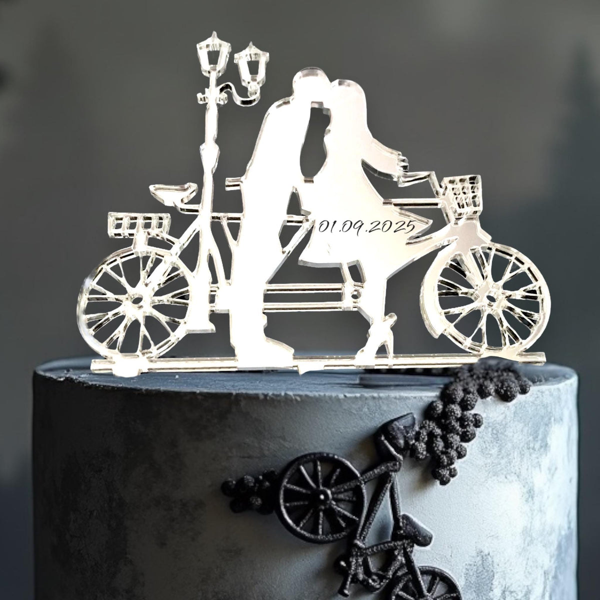 Clear acrylic cake topper of a couple on a tandem bike under a streetlamp, engraved with the date 01.09.2025.