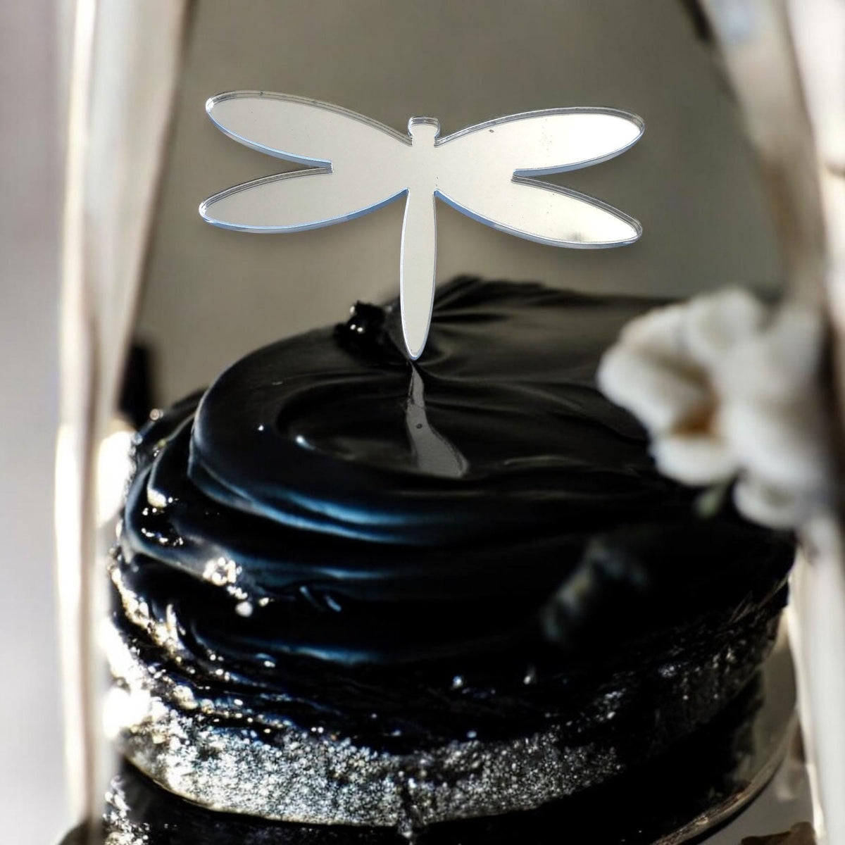 Shiny, silver, reflective dragonfly cake topper by SuperCoolCreations, styled as a minimalist silhouette on a cake.